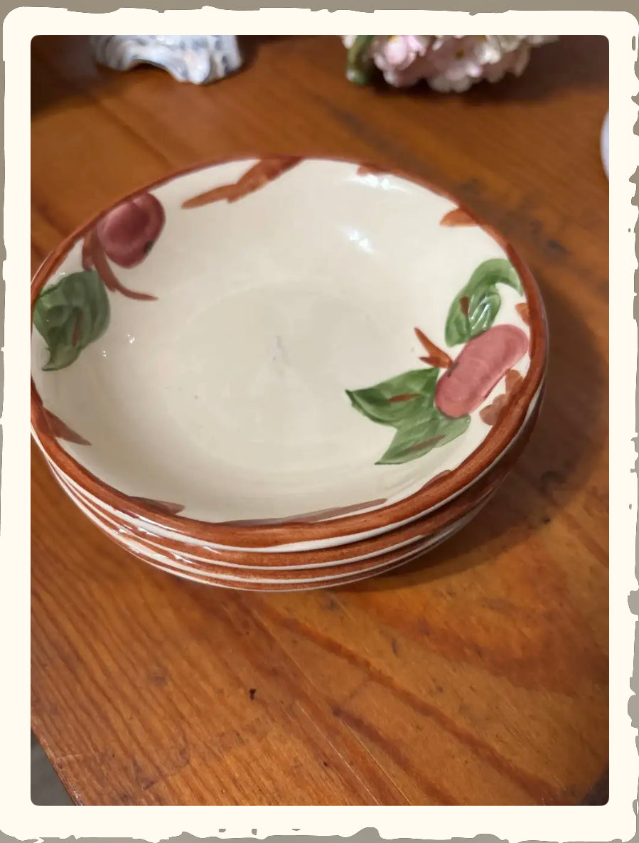 Stack of vintage Franciscan Apple pattern small bowls with hand-painted apple and leaf design on wood surface
